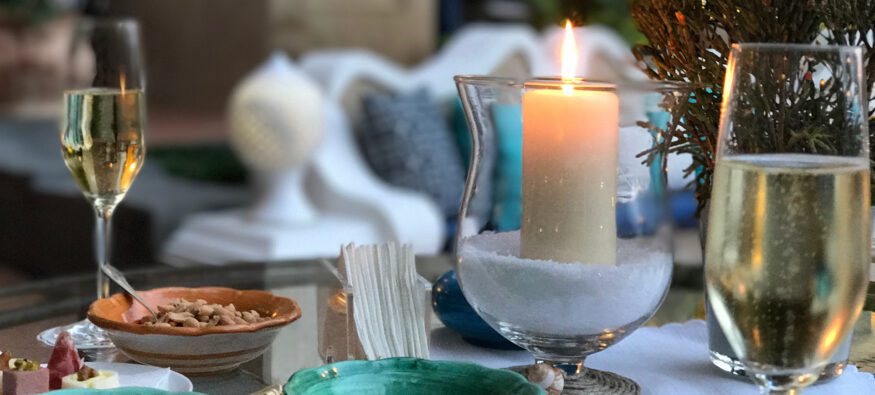 A cozy evening setting featuring two glasses of champagne, a lit candle, and small plates of snacks on a table.