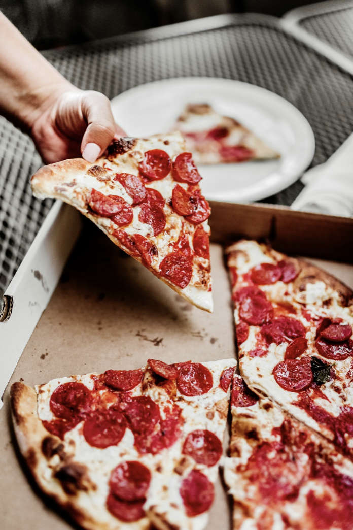 Person picking up a slice of fresh pepperoni pizza from the box on an outdoor table.